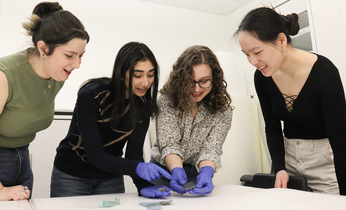 A group of four undergraduate student curators study a Lapis Lazuli rock, shaped into an axe-head